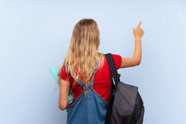 İzparmağı ile geri işaret izole mavi duvar üzerinde genç sarışın öğrenci kadın