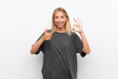 Izole beyaz arka plan üzerinde Blonde genç kadın ok işareti ve başparmak yukarı jest gösteren