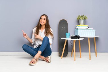 Genç bir kadın yerde oturuyor ve parmağıyla işaret ediyor.