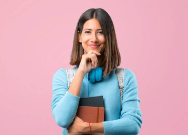 Mavi kazak ve kulaklık ile genç öğrenci kız gülümseyerek ve pembe arka plan üzerinde kendinden emin yüzü ile ön bakıyor