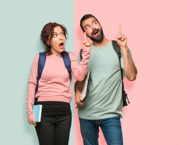 Renkli duvara parmağını kaldırırken çözümü gerçekleştirmek isteyen sırt çantaları ve kitapları olan iki öğrenci