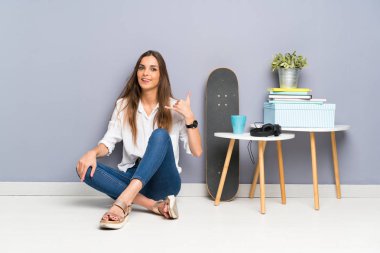 Yerde oturan ve telefon jesti yapan genç kadın