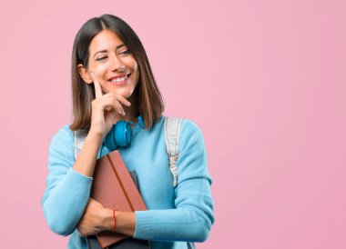 Mavi kazak ve kulaklık ayakta ve pembe arka plan üzerinde çene üzerinde el ile yan bakıyor genç öğrenci kız