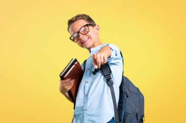 Sırt çantası ve gözlük lü öğrenci çocuk sarı arka planda sizi işaret ediyor