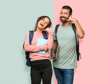 Sırt çantaları ve telefon hareketi yapan kitapları olan iki öğrenci. Renkli duvarda bana geri tabela arayın