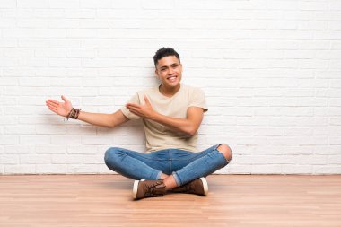 Genç adam yere oturmuş, davet edildiği için ellerini yana açıyor.