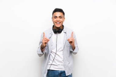 Kulaklıklı izole beyaz duvarın üzerindeki genç adam harika bir fikre işaret ediyor.