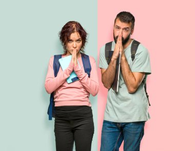 Sırt çantaları ve kitapları olan iki öğrenci avuç içi bir arada tutuyor. Kişi renkli duvarda bir şey ister