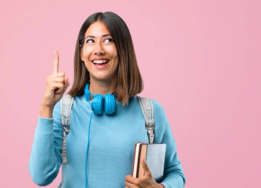 Mavi kazak ve kulaklık ile genç öğrenci kız pembe arka plan üzerinde bir parmak kaldırırken çözüm gerçekleştirmek niyetinde