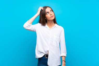 Soyutlanmış mavi arka planı olan genç bir kadın kafasını kaşırken şüpheye düşüyor.