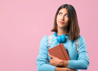 Mavi kazak ve kulaklık standı ile genç öğrenci kız ve pembe arka plan üzerinde ciddi bir yüz ile bakıyor