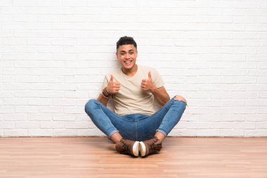 Genç adam yerde oturuyor ve baş parmak işareti yapıyor.