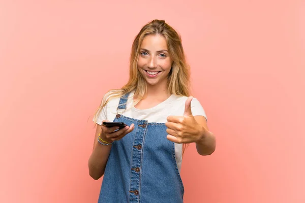 Blonďatá Mladá Žena Mobilním Telefonem Přes Izolovanou Růžovou Zeď Palci — Stock fotografie