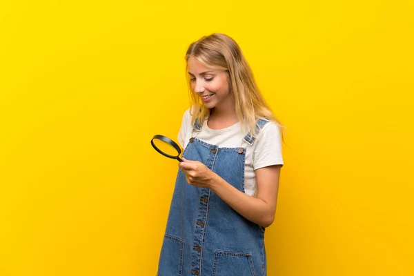 Blond Ung Kvinna Över Isolerad Gul Bakgrund Hålla Ett Förstoringsglas — Stockfoto
