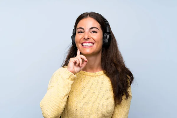 Mujer joven escuchando música con un móvil sobre una pared azul aislada — Foto de Stock