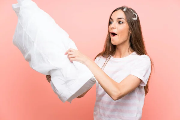 Mujer joven en pijama sobre fondo rosa aislado sosteniendo una almohada y jugando —  Fotos de Stock