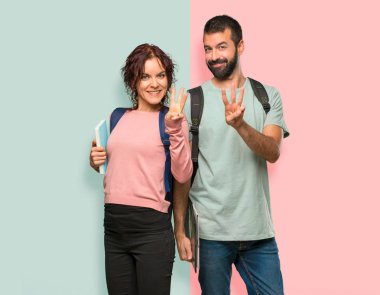 Sırt çantaları ve kitapları mutlu ve renkli duvarda parmakları ile üç sayma ile iki öğrenci