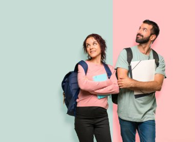 Renkli duvarda gülümseyerek sırt çantaları ve kitaplar ile iki öğrenci yukarı bakıyor