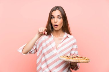 İzole pembe duvar üzerinde bir pizza tutan genç kadın şaşırttı ve ön işaret