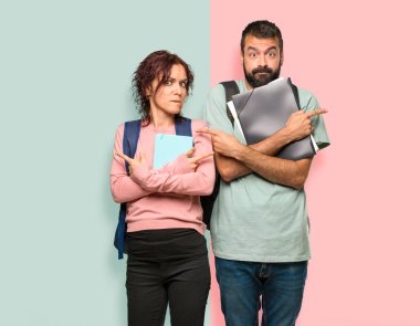 Sırt çantaları ve kitapları olan iki öğrenci, yanların şüpheleri olduğunu gösteriyor. Renkli duvarda kararsız kişi