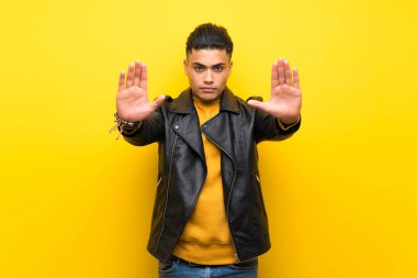 Izole sarı arka plan üzerinde genç adam stop jest yapma ve hayal kırıklığına