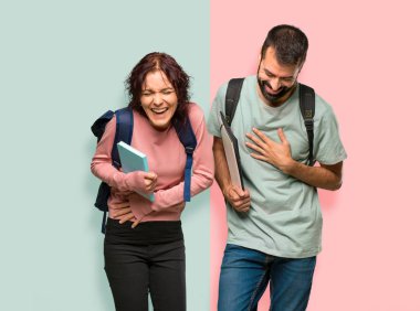 Renkli duvara ellerini göğüs koyarken sırt çantaları ve kitapları ile çok gülümseyen iki öğrenci