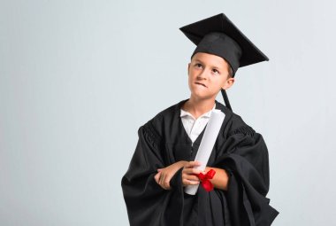 Küçük çocuk şüpheleri olan mezun ve gri arka plan üzerinde yüz ifadesi karıştırarak