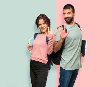 Sırt çantaları ve kitapları ile iki öğrenci renkli duvarda parmakları ile beş sayma