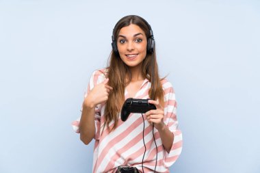 Genç kadın sürpriz yüz ifadesi ile izole mavi duvar üzerinde bir video oyunu denetleyicisi ile oynuyor