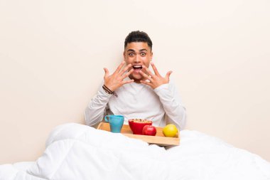 Sürpriz yüz ifadesi ile yatakta kahvaltı genç adam