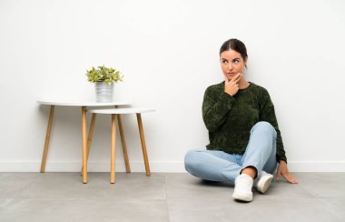 Genç bir kadın yerde oturmuş bir fikir düşünüyor.