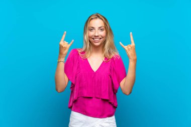 Izole mavi arka plan üzerinde sarışın genç kadın rock jest yapma