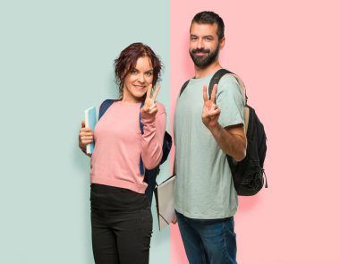 Sırt çantaları ve kitapları mutlu ve renkli duvarda parmakları ile iki sayma ile iki öğrenci