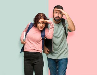 Sırt çantaları ve kitapları ile iki öğrenci el ile renkli duvarda bir şey bakmak için uzak bakıyor