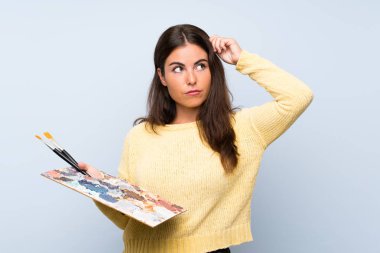 Izole mavi arka plan üzerinde genç sanatçı kadın şüpheler ve yüz ifadesi karıştırarak sahip