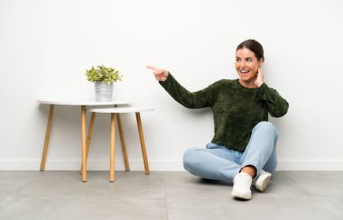 Genç bir kadın yerde oturuyor ve parmağıyla işaret ediyor.