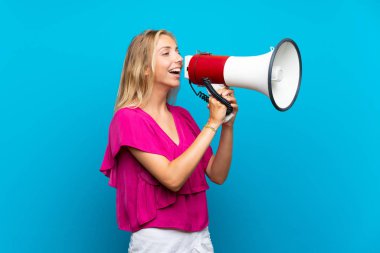 Izole mavi arka plan üzerinde sarışın genç kadın bir megafon ile bağırarak