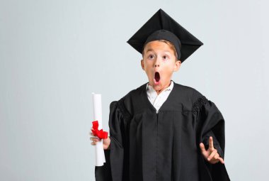 Küçük çocuk mezun gri arka plan üzerinde komik ve çılgın yüz duygu yapar