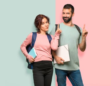 Sırt çantaları ve kitapları ile iki öğrenci gösteren ve renkli duvarda en iyi işareti bir parmak kaldırma