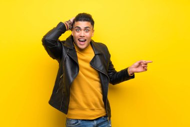 Izole sarı arka plan üzerinde genç adam şaşırttı ve yan parmak işaret