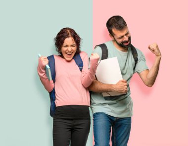 Sırt çantaları ve kitapları ile iki öğrenci bir zafer kutluyor ve renkli duvarda bir ödül kazanmış olması için mutlu