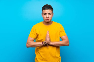 Izole mavi arka plan üzerinde sarı gömlekli genç adam birlikte palmiye tutar. Kişi bir şey ister