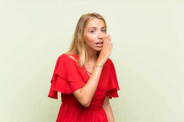 Izole yeşil arka plan üzerinde sarışın genç kadın bir şey fısıldıyor