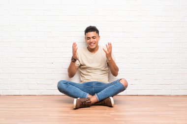 Genç adam yerde oturmuş gülüyor.