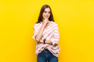 İzole edilmiş sarı arka planı olan genç bir kadın yan tarafa bakıyor.