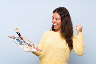 İzole mavi arka plan üzerinde genç sanatçı kadın bir zafer kutluyor