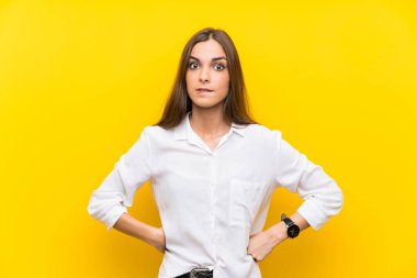 İzole edilmiş sarı arka planı olan genç bir kadın. Şüpheleri var ve kafası karışmış bir yüz ifadesi var.