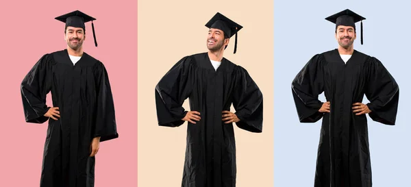 卒業式の日に男のセット大学は腰に腕を持ってポーズをとり カラフルな背景に笑う — ストック写真