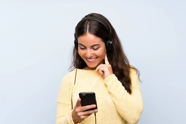 Jeune femme écoutant de la musique avec un mobile sur un mur bleu isolé — Photo