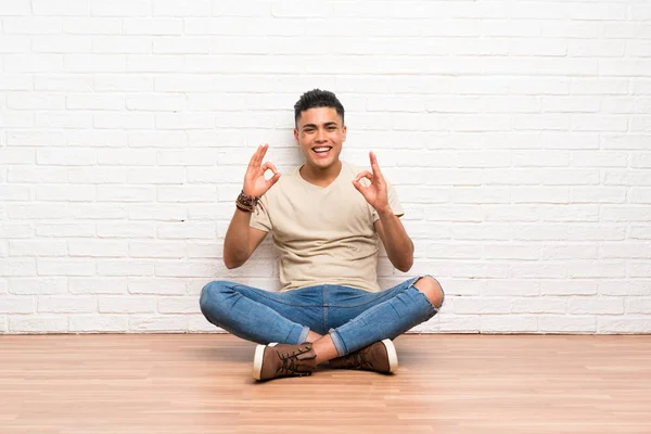 Νέος Άνθρωπος Κάθεται Στο Πάτωμα Δείχνοντας Ένα Πινακίδα Δάχτυλα — Φωτογραφία Αρχείου